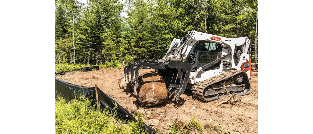 Bobcat compact track loader with a root grapple attachment moving large boulders for site preparation and lot clearing in Roseburg, Oregon.